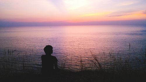 Silhouette man by sea against sky during sunset