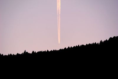 Low angle view of silhouette vapor trail against clear sky