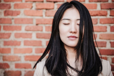 Relaxed beautiful chinese business woman standing over bricks wall background with eyes closed