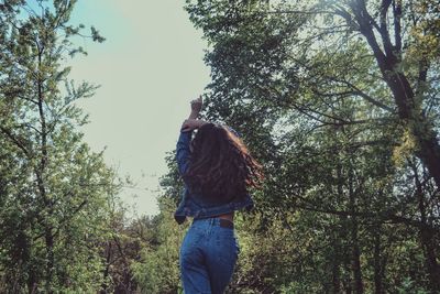 Rear view of young woman standing by trees in forest
