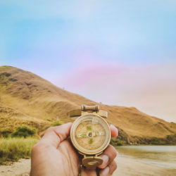 Cropped hand holding navigational compass against sky