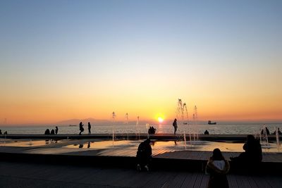 Silhouette people on beach against clear sky during sunset