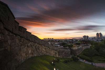 Fortified wall in city against sky during sunset