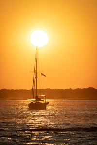 Silhouette sailboat in sea against orange sky