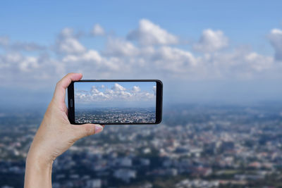 Man photographing with mobile phone against sky