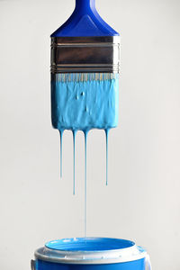 Close-up of blue paint dripping into container against wall