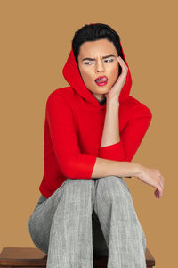 Portrait of young woman sitting against pink background