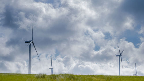 Low angle view of windmills on field against sky