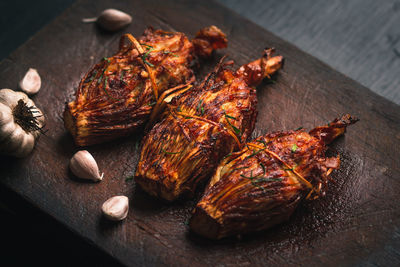 High angle view of chicken meat with garlic cloves served on wooden tray