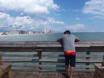 Rear view of woman standing on pier by sea against sky