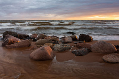 Rocks on beach against sky during sunset