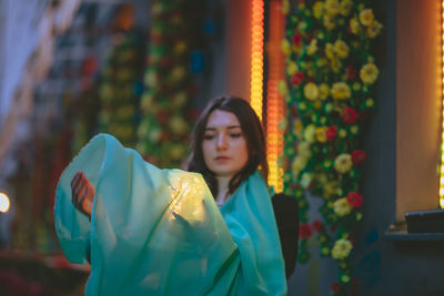 Beautiful woman holding scarf and glowing jar against building at dusk