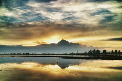 Scenic view of lake against cloudy sky at sunset