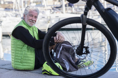 Portrait of man sitting by bicycle at harbor