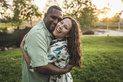 Portrait of cheerful couple embracing on field at park