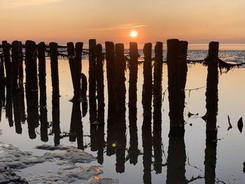 Silhouette wooden posts on beach against sky during sunset