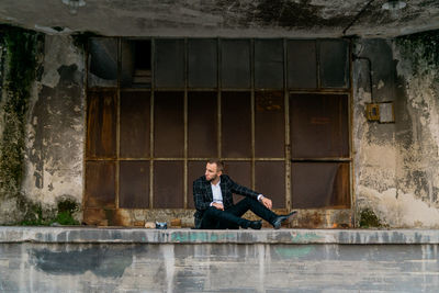 Young man looking away while sitting against old building