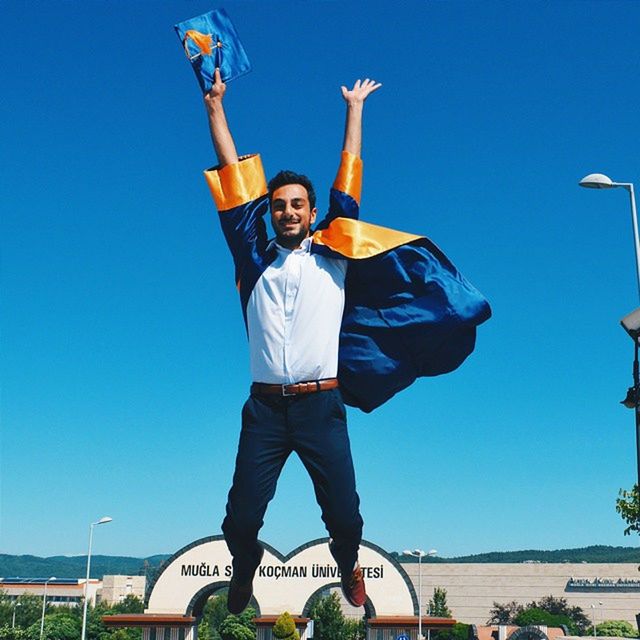 blue, clear sky, lifestyles, casual clothing, young men, leisure activity, full length, person, young adult, front view, portrait, looking at camera, low angle view, standing, copy space, mid-air, smiling, happiness