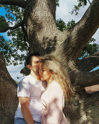 Portrait of young couple standing under shadow of tree  in park