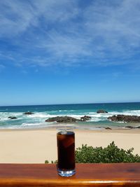 Glass of coffee on beach against sky