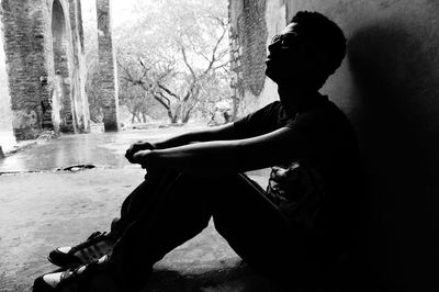 Silhouette of man wearing sunglasses looking up while sitting against wall