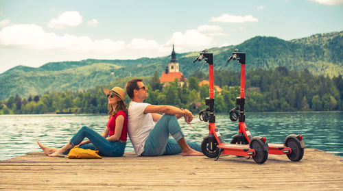 People sitting by lake against sky