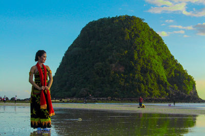 Full length of woman standing against rock formation on beach against sky