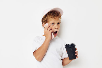 Boy holding disposable cup while talking on phone against white background