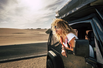 Woman with blond hair looking through window while traveling in off-road vehicle