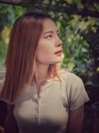 Young woman looking away against tree