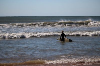 Rear view of a surfer walking on beach