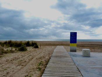 Wooden post on footpath by sea against sky