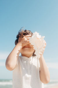 Close-up of girl holding seashell standing against sky