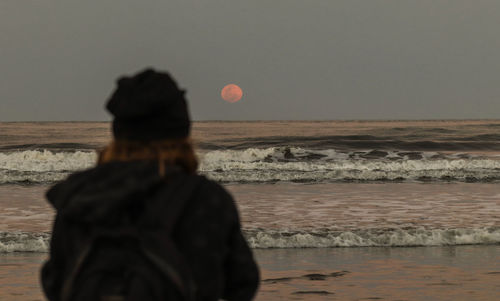 Rear view of woman standing on beach against clear sky