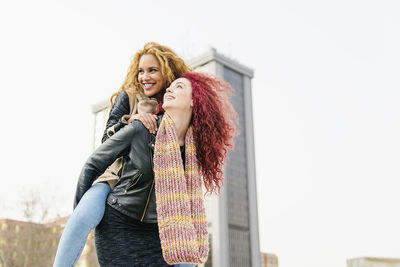 Low angle view of woman piggybacking girlfriend against clear sky