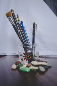 Close-up of paintbrushes and pens in glass container on table