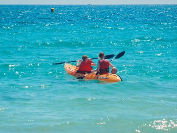 Father assisting children in rowing kayak at sea