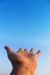 Low angle view of hand against clear blue sky