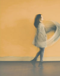 Blurred motion of woman walking by yellow wall