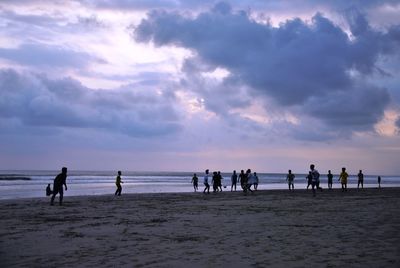 Male friends playing soccer at beach against cloudy sky