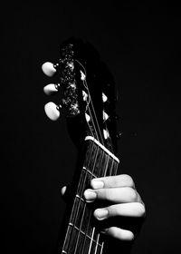 Close-up of hand holding guitar against black background