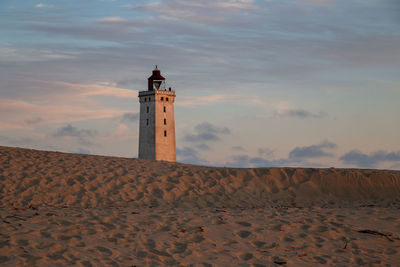 Lighthouse on beach against sky during sunset