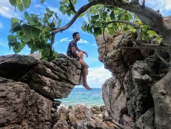 Side view of man on rock by sea against sky