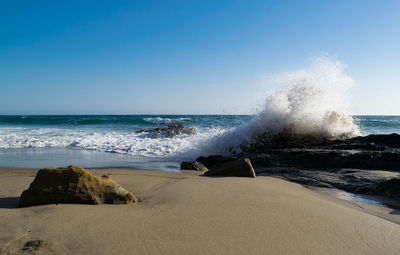 Wave splashing on rock formation at beach against clear sky