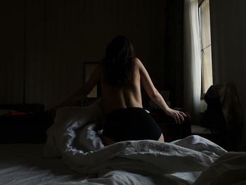 Rear view of topless woman sitting on bed at home