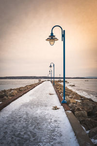 Street light by sea against sky during sunset