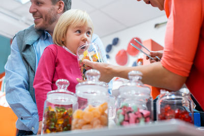 Sales clerk holding jar with candies by girl at store