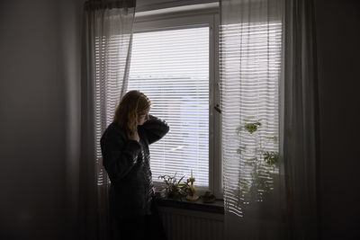 Pensive teenage girl looking through window