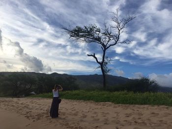 Bare trees on landscape against cloudy sky