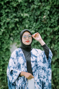 Portrait of young woman wearing sunglasses while standing against trees